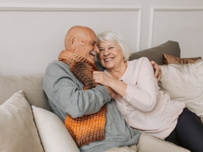 A happy elderly couple sits on the couch and smiles