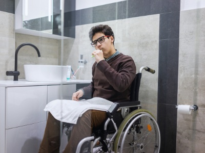 A man in a wheelchair brushes his teeth in renovated bathroom